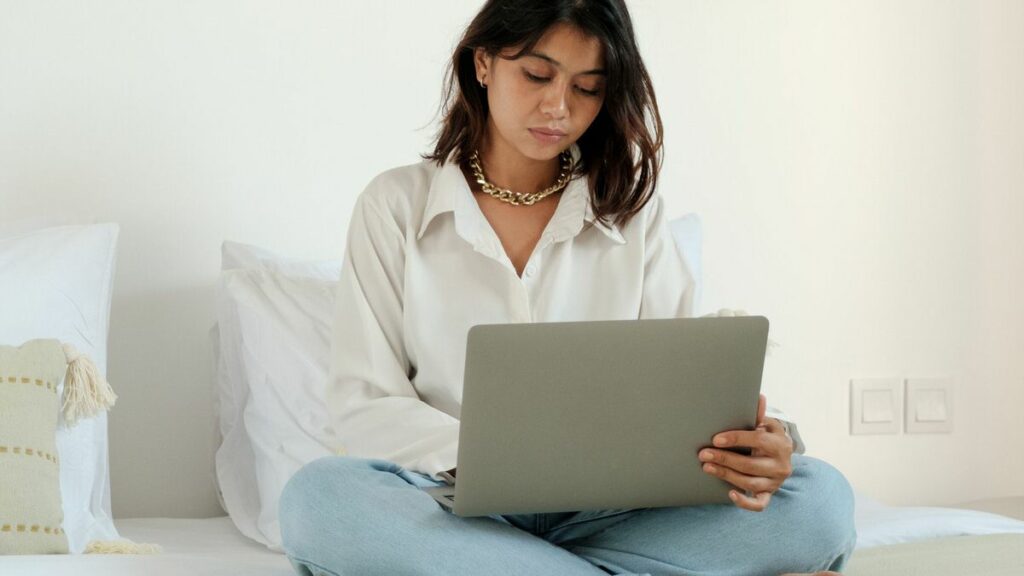 A woman sitting on a bed with a laptop open on her lap. 