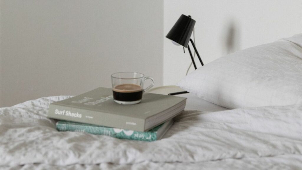 A cup of coffee sitting on books that are on a bed. 